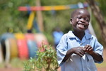 Laughing boy playing outside child-friendly classroom supported by Plan